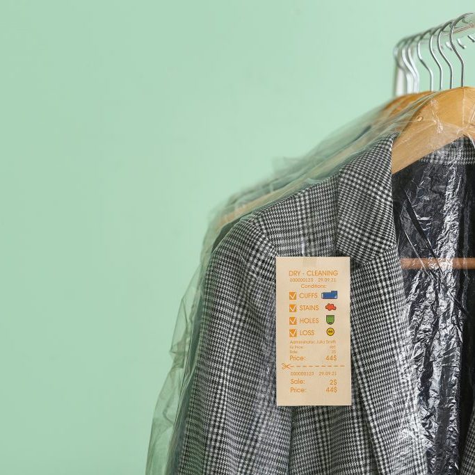 Rack with clean checkered jacket in plastic bag on green background, closeup